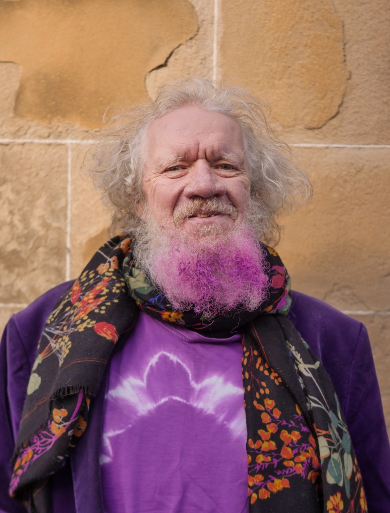 Photo of the bearded David Renton wearing a scarf and tie dye purple shirt. 