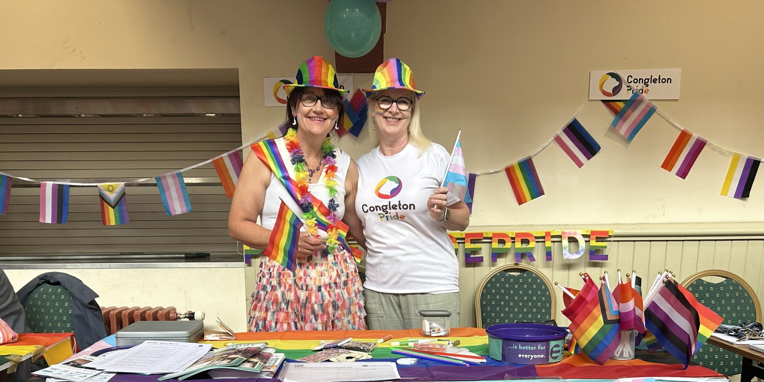 Two women on a Pride stall waving rainbow flags